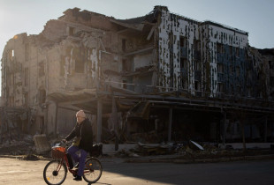 Një banore vendëse kalon me biçikletë pranë një dyqani dhe restoranti të shkatërruar në qytetin e Ukrianës, Pokrovsk, më 19 nëntor 2024.