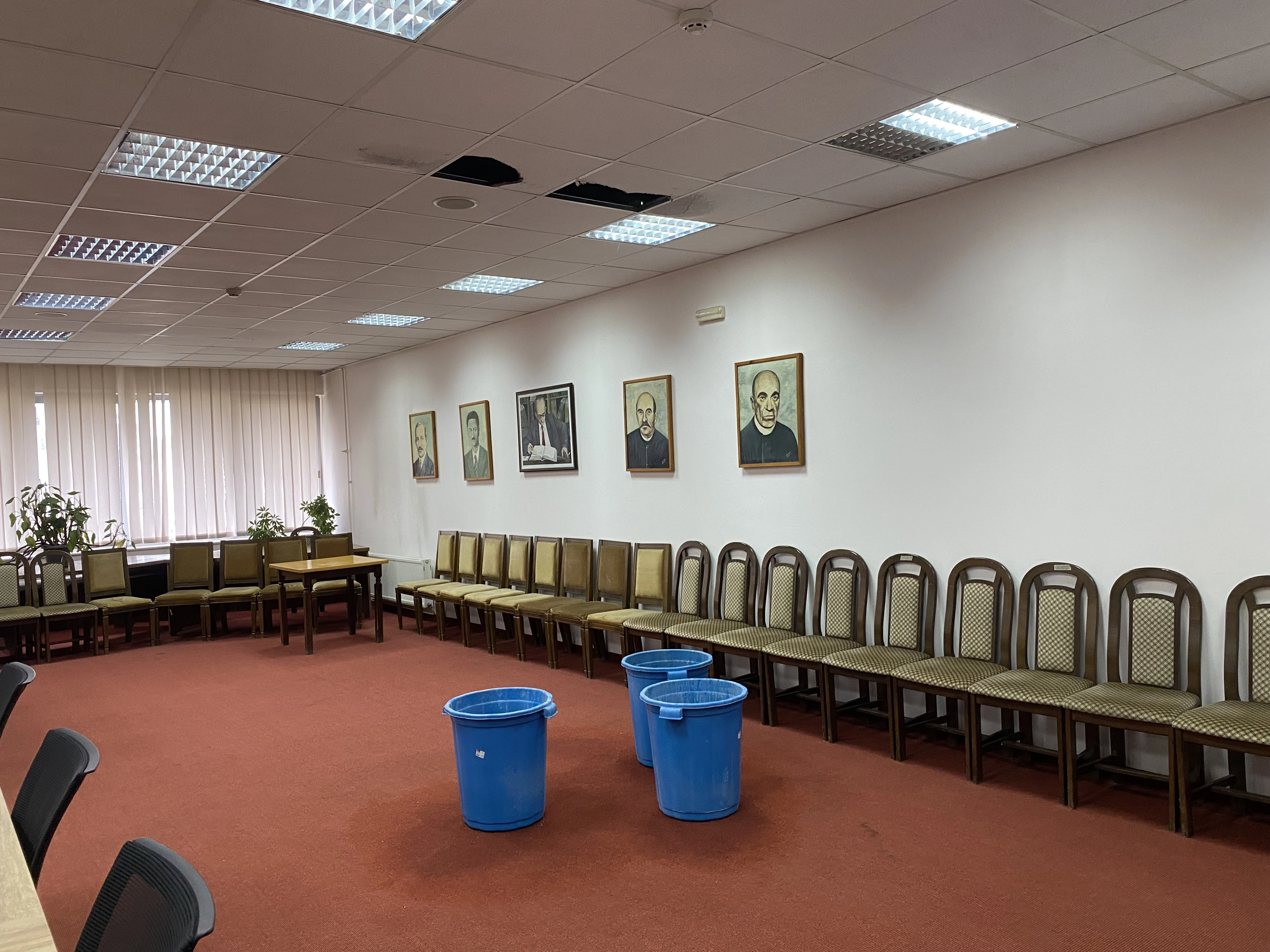 Në sallën e konferencave, aty ku prej vitesh janë mbajtur mbledhjet, ligjëratat e prezantimet shkencore, në ditët me shi, tri kova të mëdha plastike qëndrojnë në qendër të tapetit të kuq duke mbledhur ujin që pikon